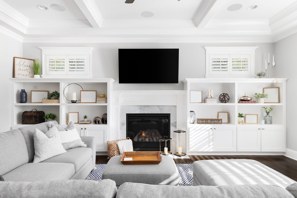 A beautiful, bright living room with a large sectional sofa, television hanging over a fireplace, and built-in shelving with decorations.