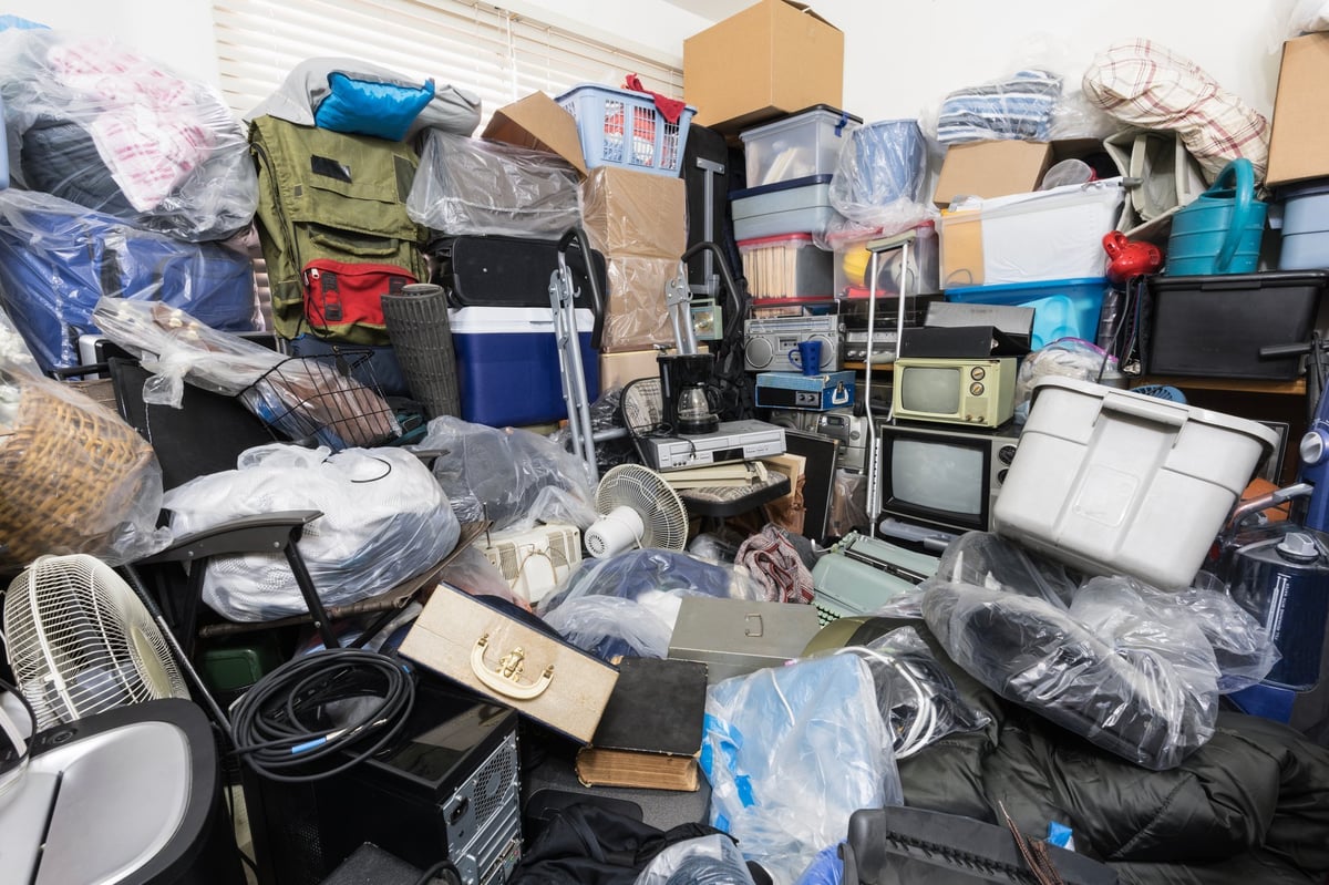 Hoarder house bedroom packed with clothing bags, household objects, vintage electronics and miscellaneous junk.