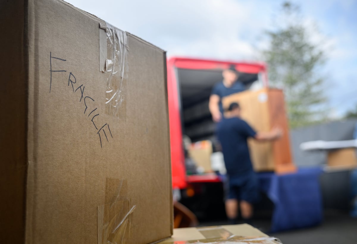 Hand-written word Fragile on the cardboard box. Unrecognizable people loading furniture to the pickup truck. Concept of home moving and delivery.