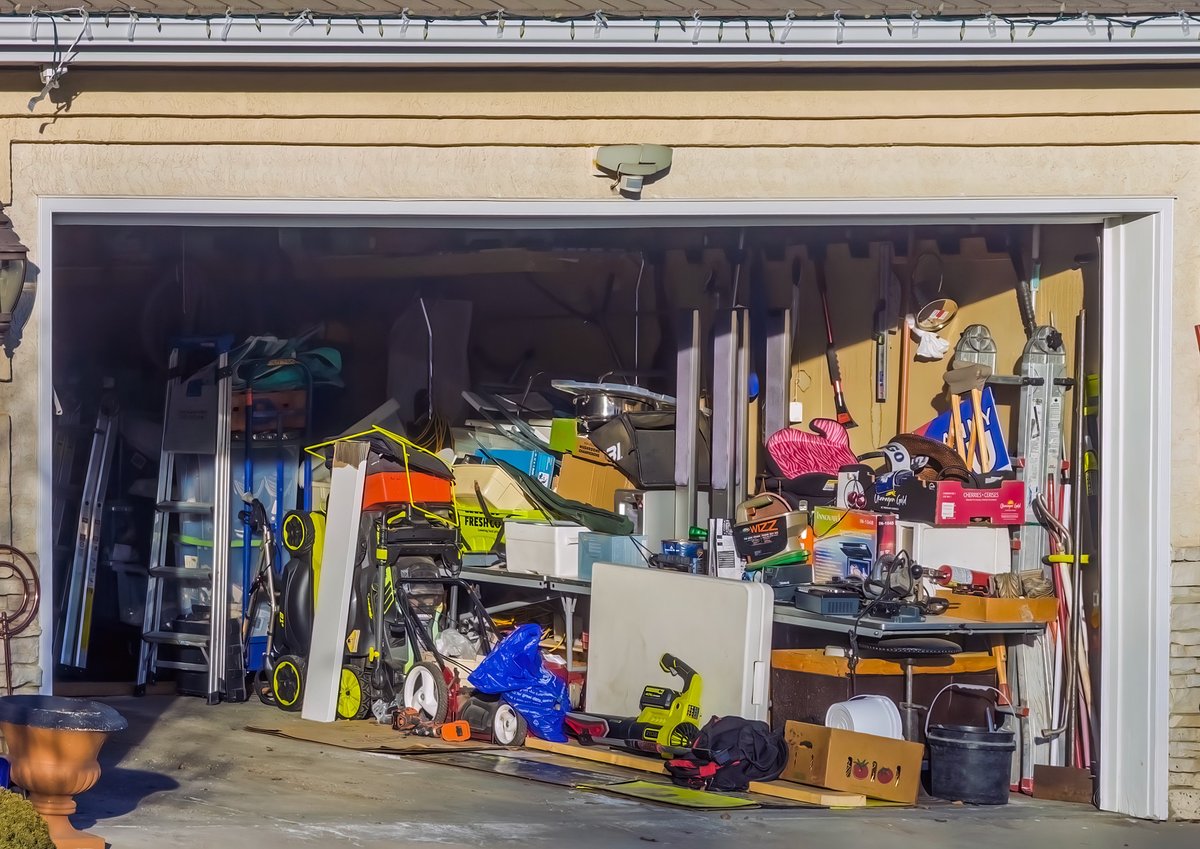 Calgary, Alberta, Canada. Jan 18, 2026. A cluttered suburban garage filled with overflowing household items, lawn equipment, and tools.