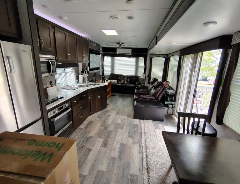 Interior of a modern RV showing kitchen with dark cabinets, dining area, and seating with large windows