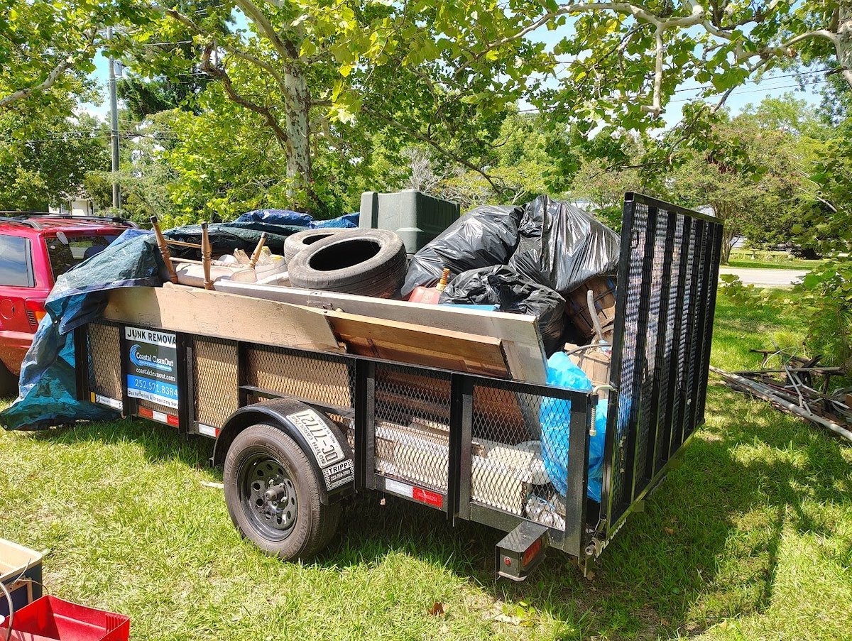 Utility trailer loaded with scrap metal, tires, and waste materials in a grassy outdoor area