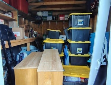Interior of a service van with wooden storage shelves, black storage containers stacked on yellow platform, and tools mounted on walls.