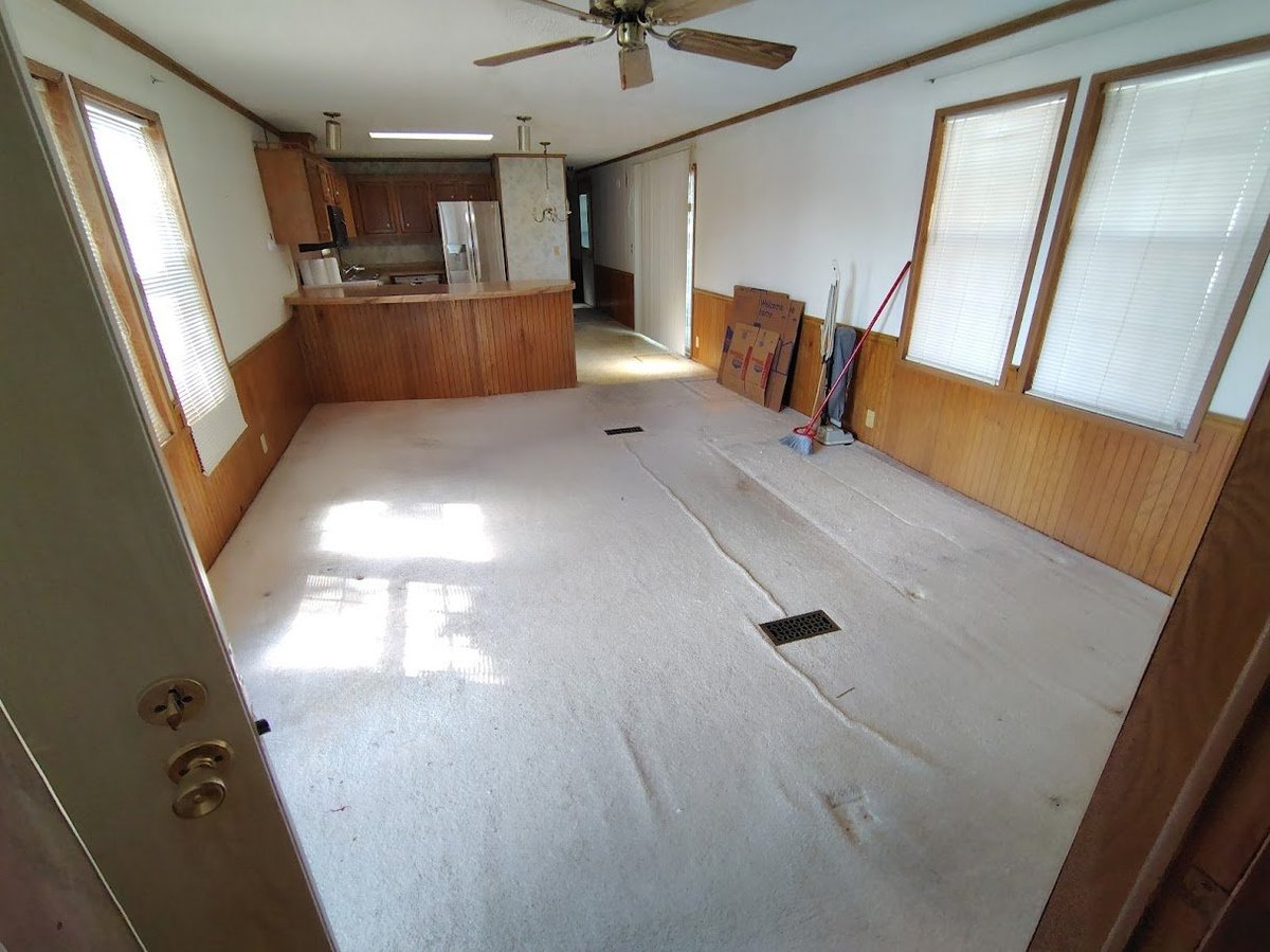 Empty interior room with wooden wall paneling, white floor covered in protective sheeting, wood-trimmed windows, and ceiling fan