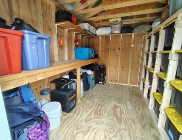 Interior of a wooden storage shed with shelves holding colorful bins and organized items along the walls.