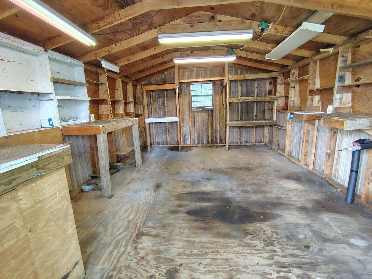 Empty wooden barn interior with exposed beams, work tables, shelving, and concrete floor