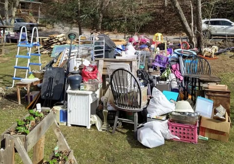 Outdoor yard sale displaying assorted furniture, household items, and miscellaneous goods spread across a grassy area