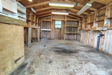 Empty wooden barn interior with exposed beam ceiling, brick walls, and wooden stalls on sides